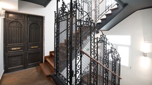 Una escalera con barandillas de metal ornamentadas y un pasamanos de madera que lleva a un rellano con una puerta de madera oscura.