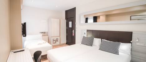 Ein Hotelzimmer mit einem großen Bett, einem Einzelbett, einem Schreibtisch mit Stuhl, einem Kleiderschrank und einem Fernseher.