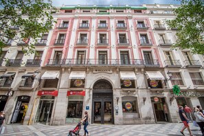 Un immeuble à plusieurs étages doté d’une entrée centrale, de devantures de magasins pour Burger King et Petit Palace, et d’une enseigne de pharmacie bien visible.