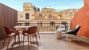 Una terraza de madera con una mesa y sillas, una silla de mimbre, y edificios a lo lejos.