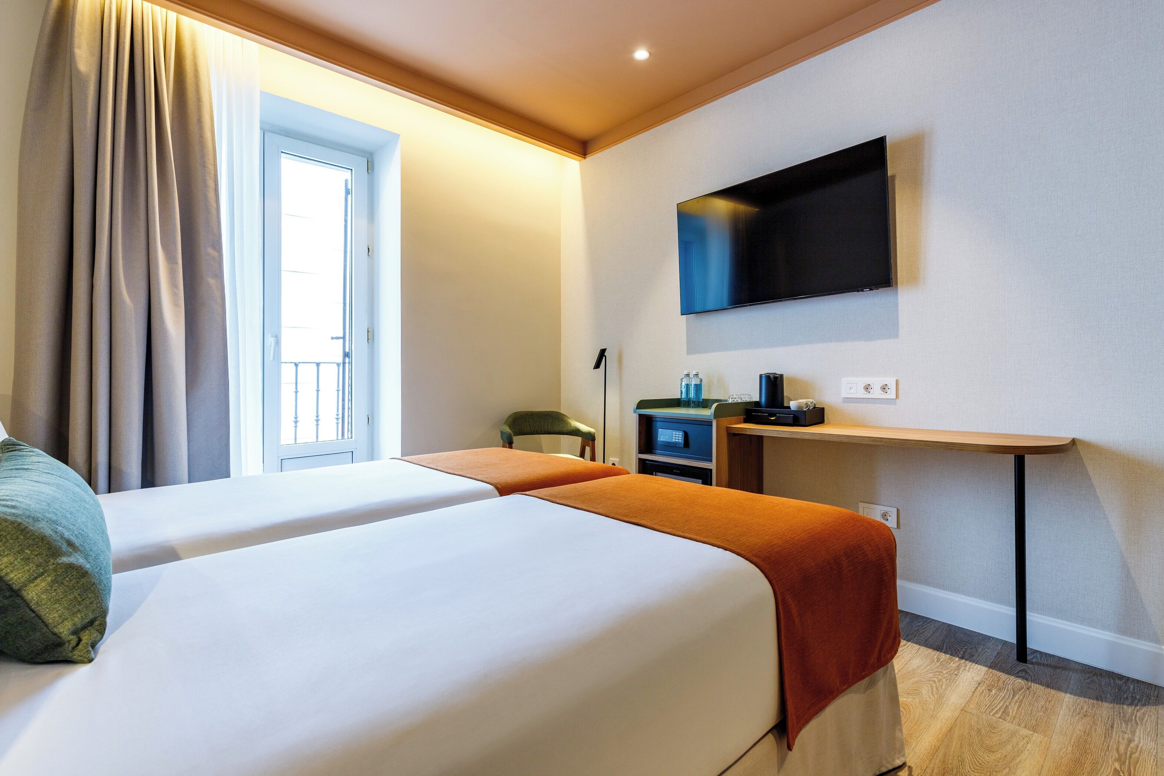 A hotel room with two beds, a TV mounted on the wall, and a desk with a chair.