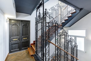 Un escalier orné de rampes en métal noir, avec une main courante en bois et une porte en bois sombre dotée de poignées en laiton.
