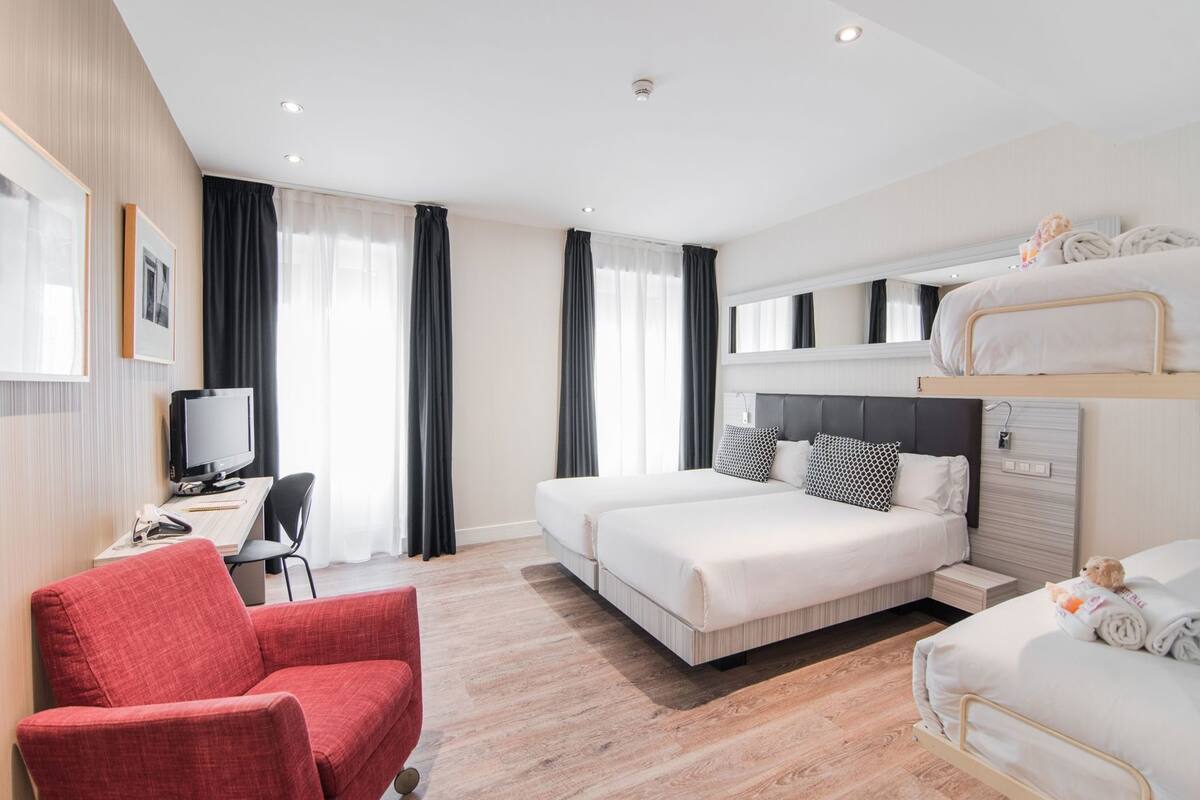 Ein Hotelzimmer mit einem Bett, einem Schreibtisch mit Computer, einem Sessel und einem Fernseher.
