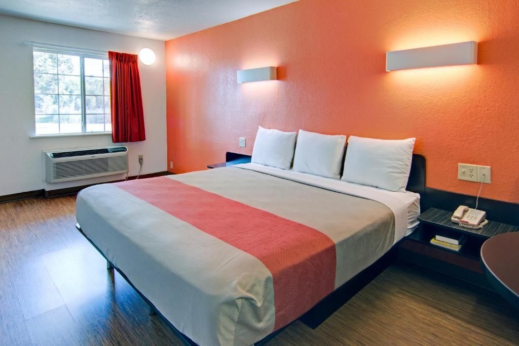 A hotel room with a bed, a nightstand, a telephone, and a window with a red curtain.