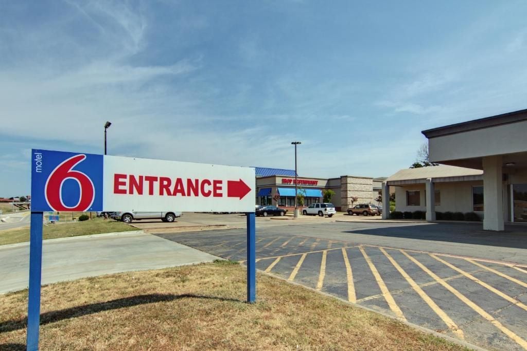 A motel entrance sign with a directional arrow, a parking lot with marked spaces, and a building with a blue awning.
