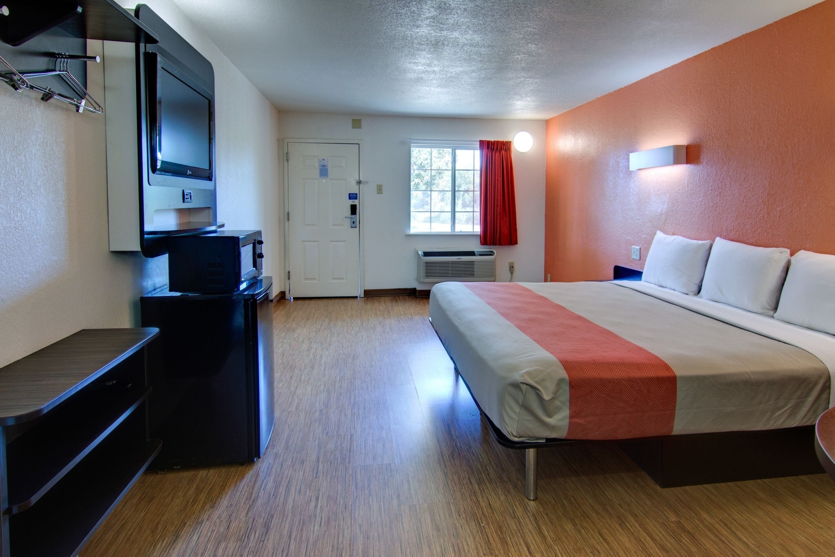 Una habitación de hotel con cama, escritorio, televisor y ventana con cortinas.