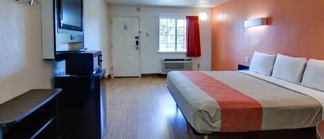 Una habitación de hotel con cama, escritorio, televisor y ventana con cortinas.