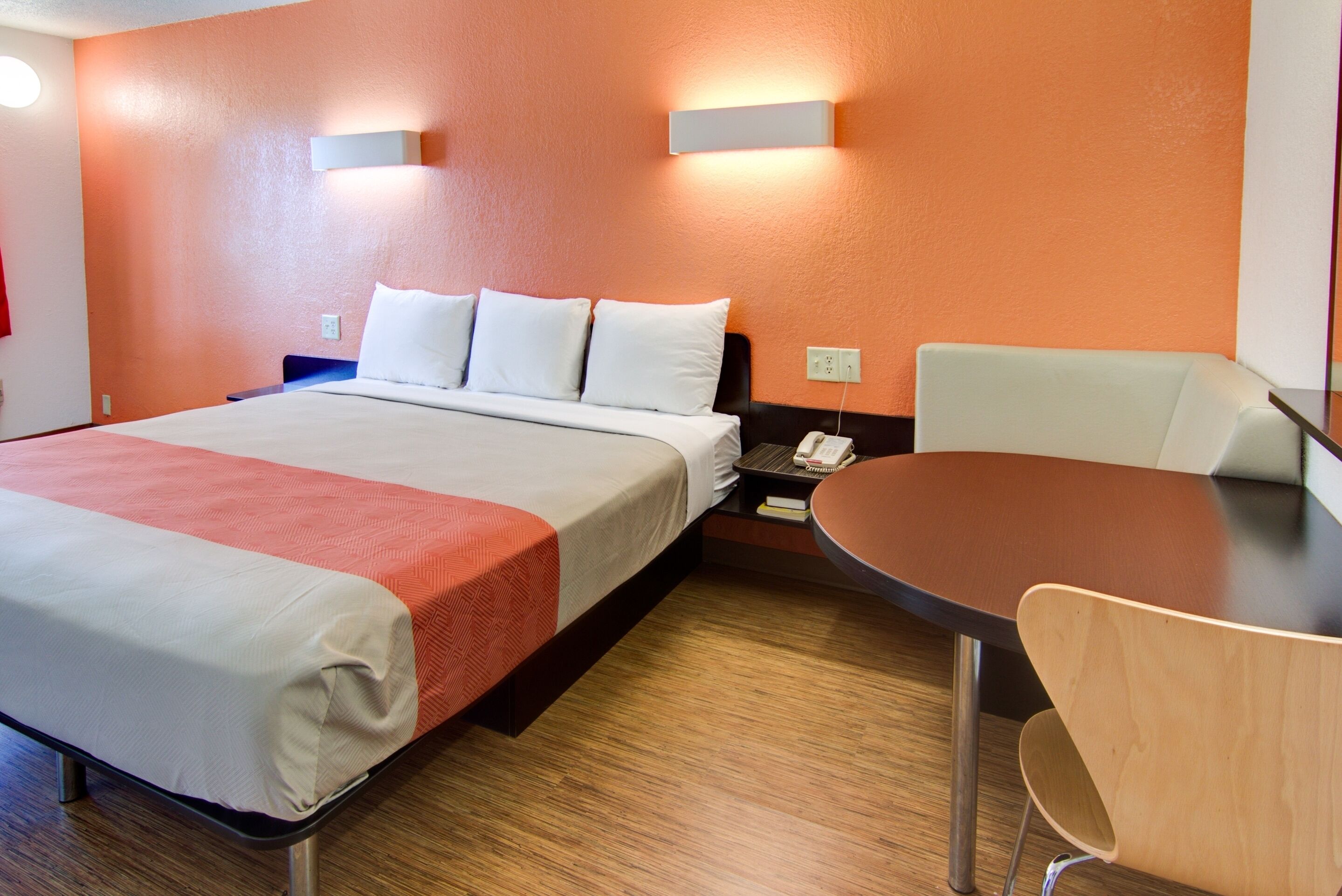 A hotel room with a bed, bedside table, chair, and a small table.