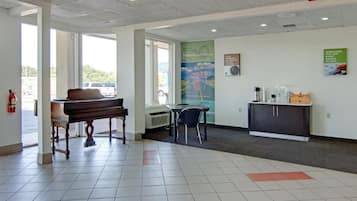 Un área de recepción con un piano, una mesa, sillas, un tablón de anuncios y un armario.