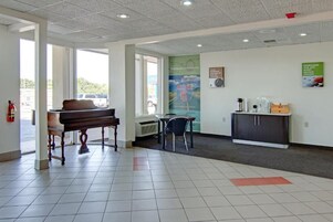 A reception area with a piano, a table, chairs, a bulletin board, and a cabinet.