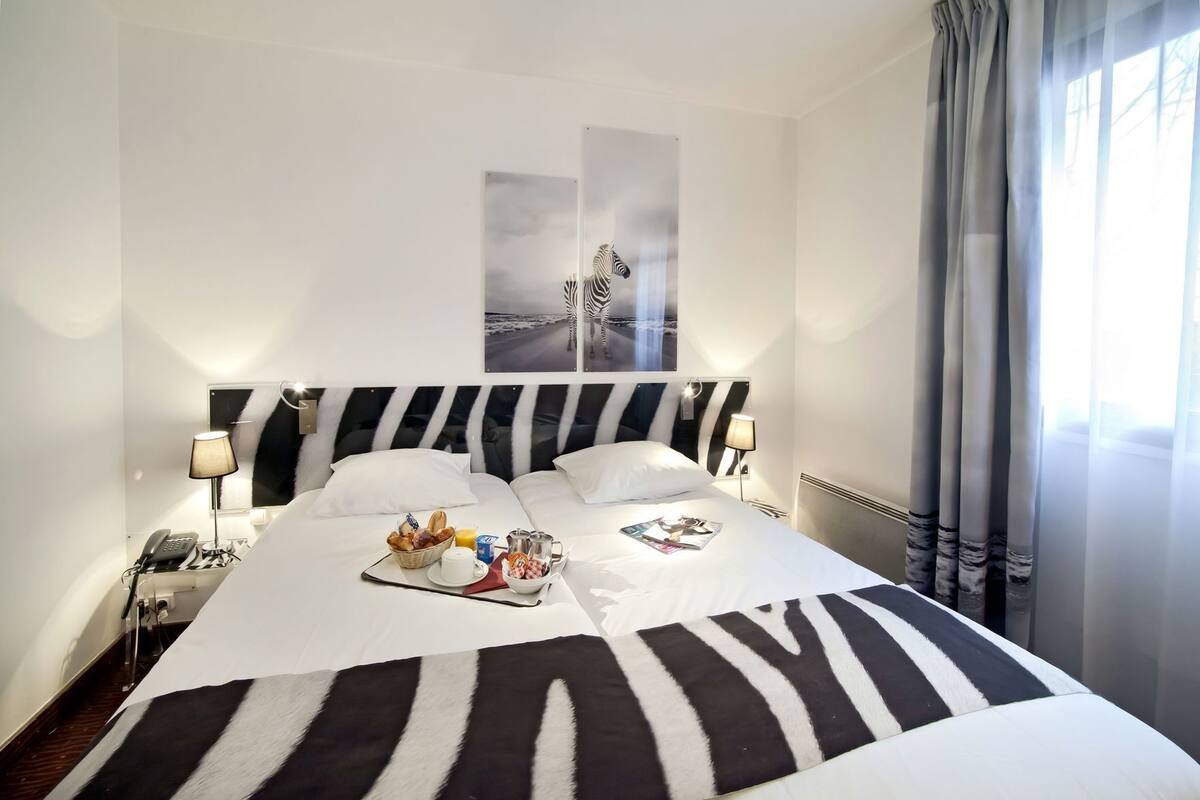 A hotel room with a zebra-striped bedspread, a breakfast tray on the bed, a mounted zebra picture on the wall, and a bedside lamp.