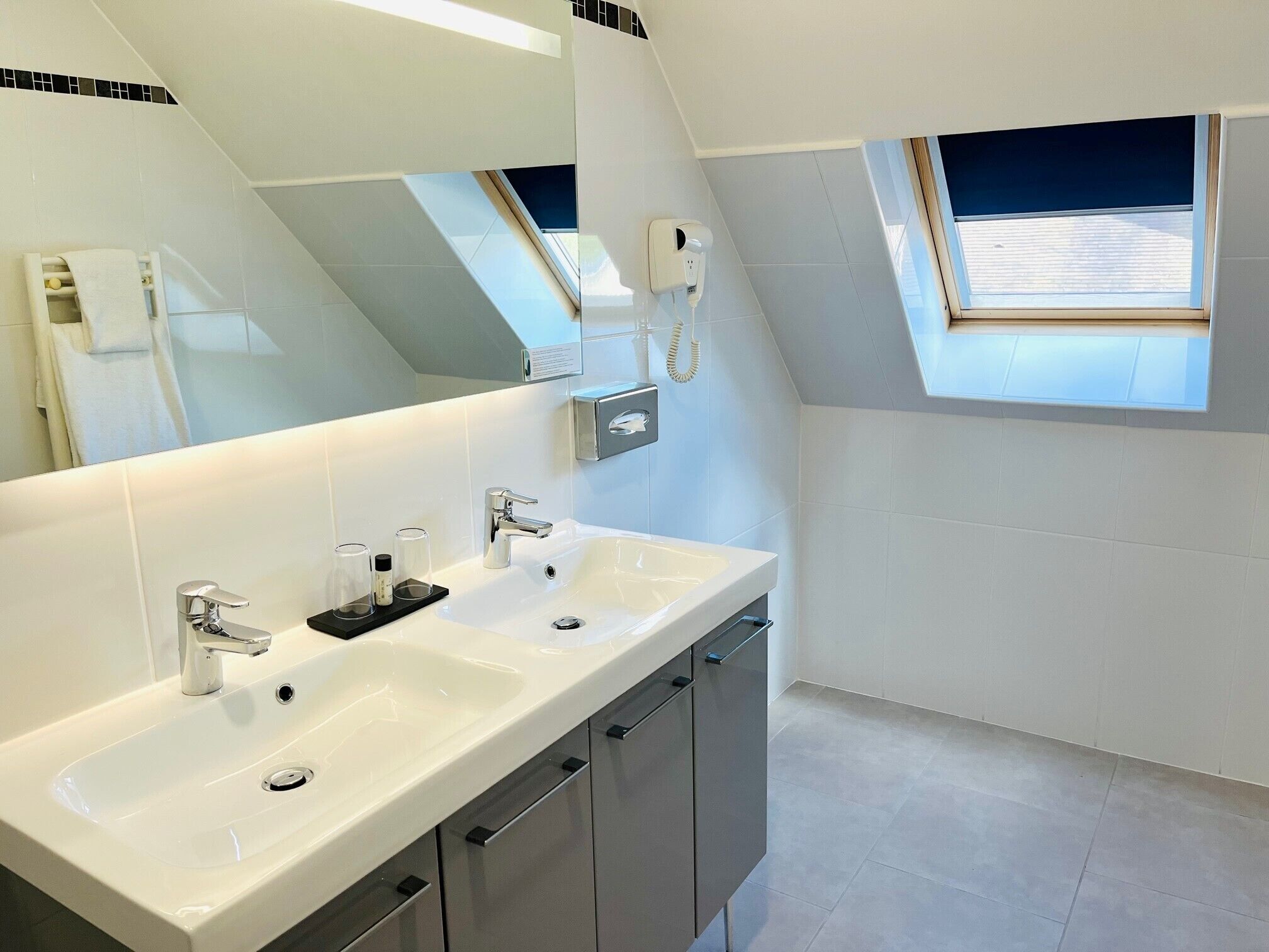 Un baño moderno con dos lavamanos, un espejo grande y un tragaluz.