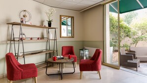 Une pièce avec une table ronde, deux chaises rouges, une bibliothèque, un miroir et une vue sur l’extérieur.