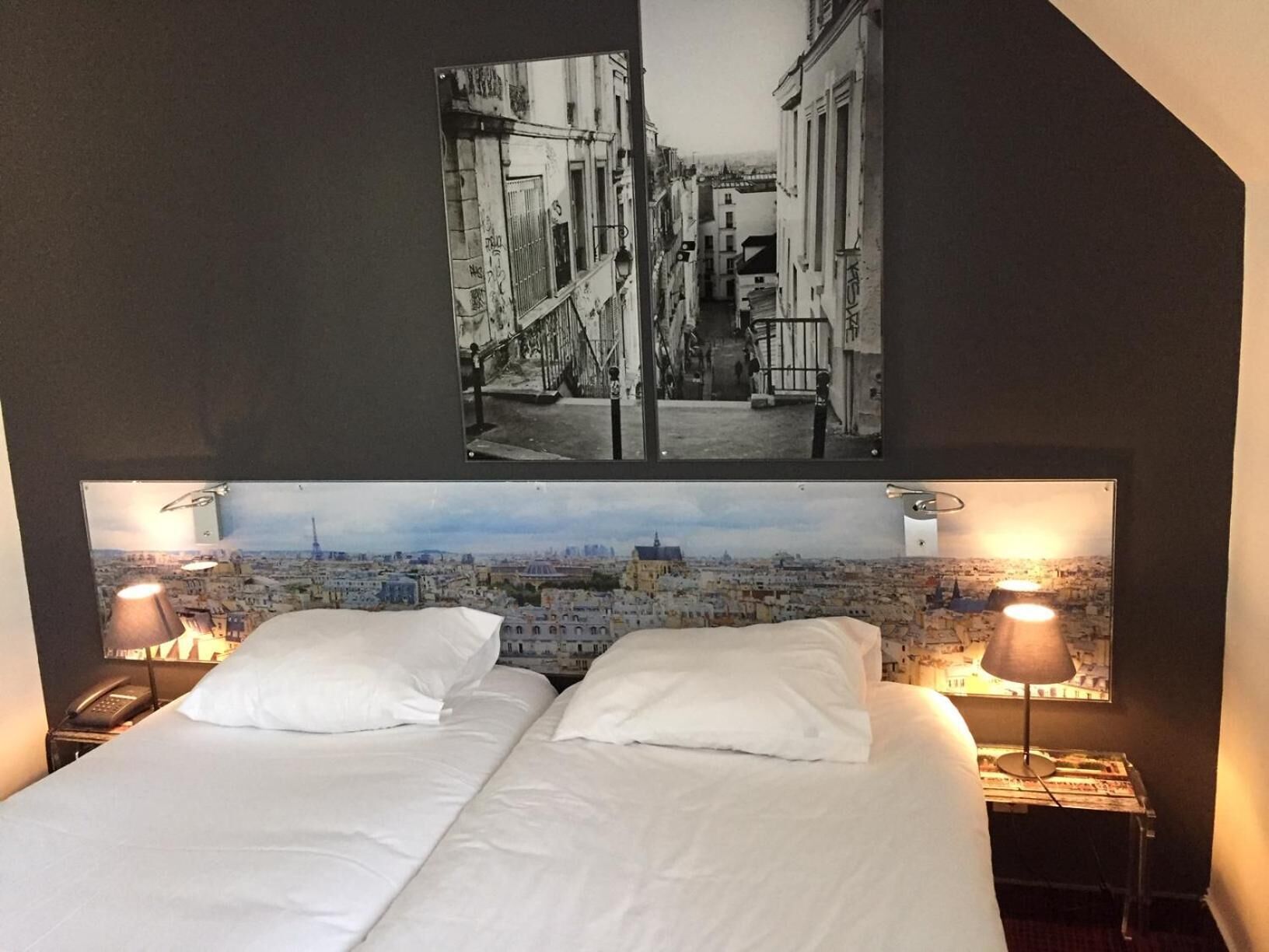 A hotel room with two beds, a cityscape view, and a framed photograph on the wall.