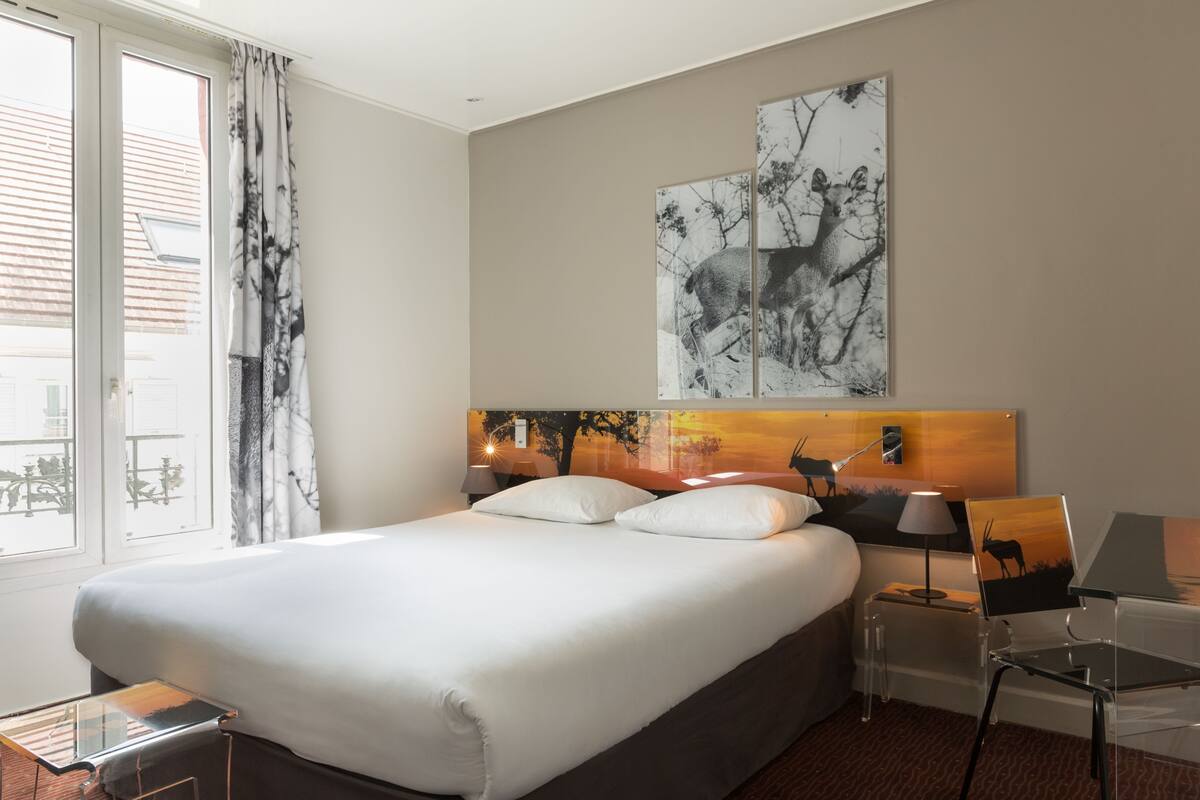 A hotel room with a large bed, a desk, a chair, and a window with curtains.