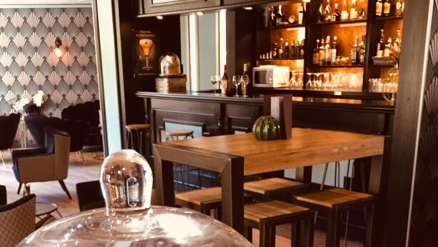 Un espace repas comprenant une grande table, des chaises et un bar avec des étagères remplies de bouteilles.