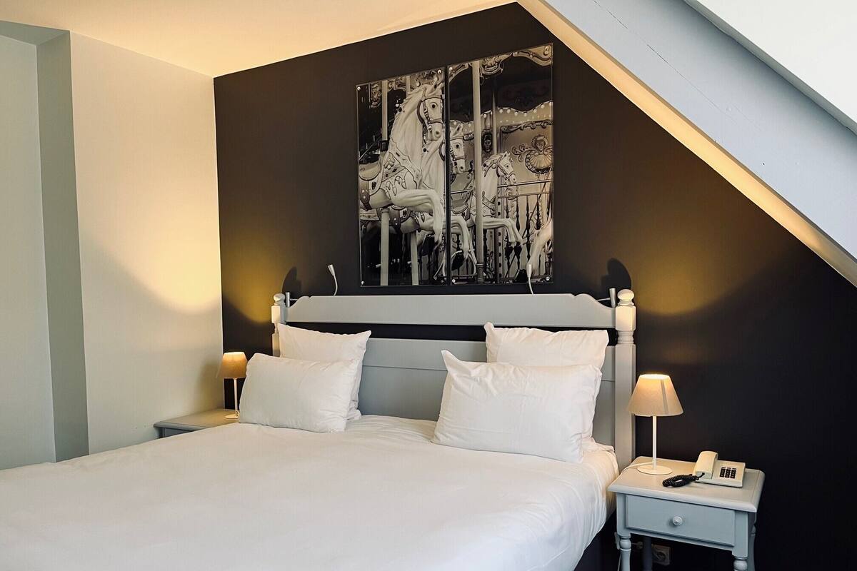 A bedroom with a bed, two bedside tables, a nightstand, and a large black and white artwork on the wall.