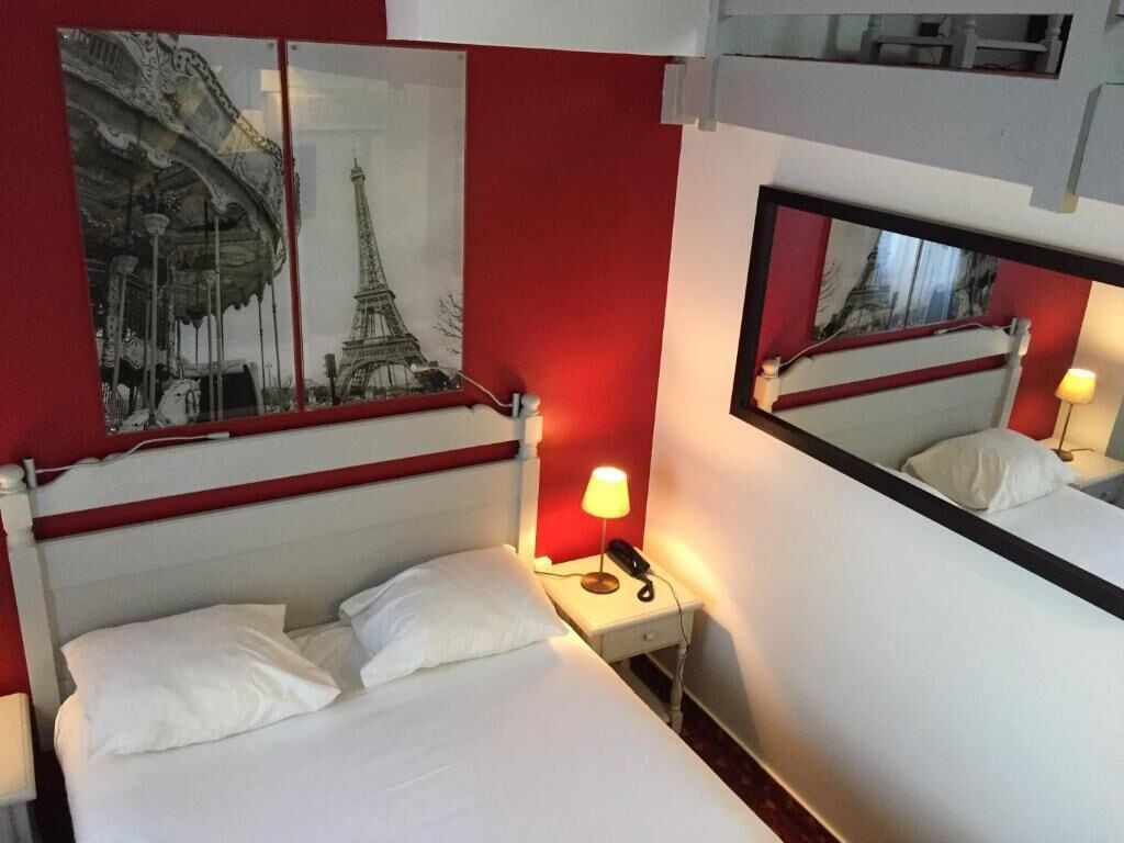 A hotel room with a bed, a nightstand with a lamp, a phone, and a mirror.