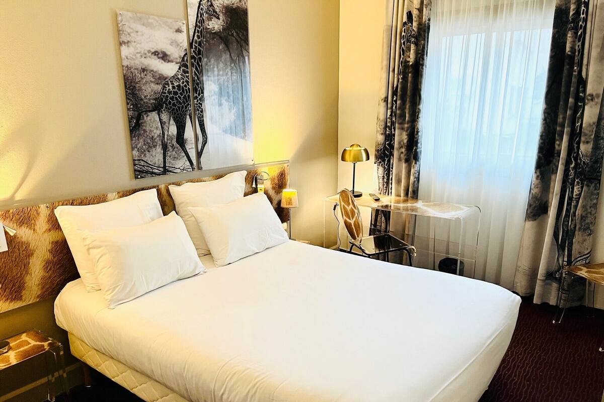 A hotel room with a large bed, a desk with a chair, a lamp, and a painting on the wall.