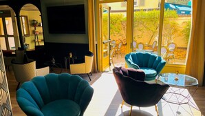 Un intérieur moderne avec des fauteuils turquoise, une table basse en verre et un téléviseur fixé au mur.