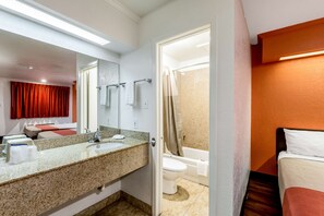 Un baño de hotel con lavamanos, espejo, inodoro y ducha.