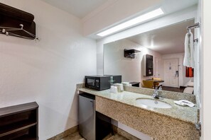 Een compacte hotelbadkamer met een granieten aanrecht, een wastafel, een spiegel, een magnetron en een kleine koelkast.