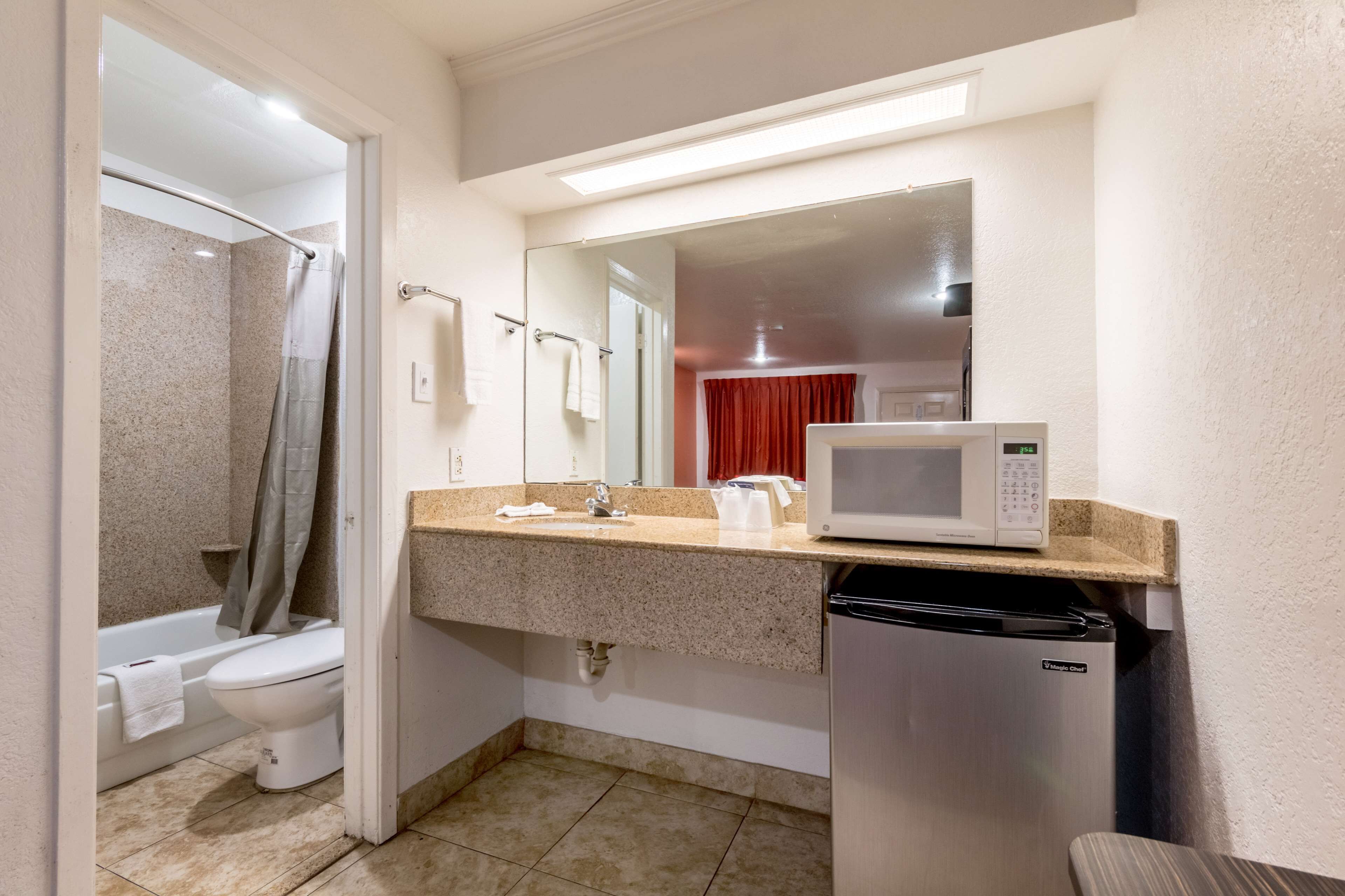 A bathroom with a toilet, shower, sink, and a microwave on a countertop.