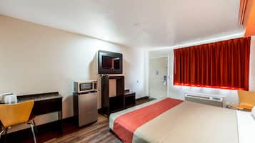 A hotel room with a bed, a desk with a computer, a microwave, a TV, and a red curtain.
