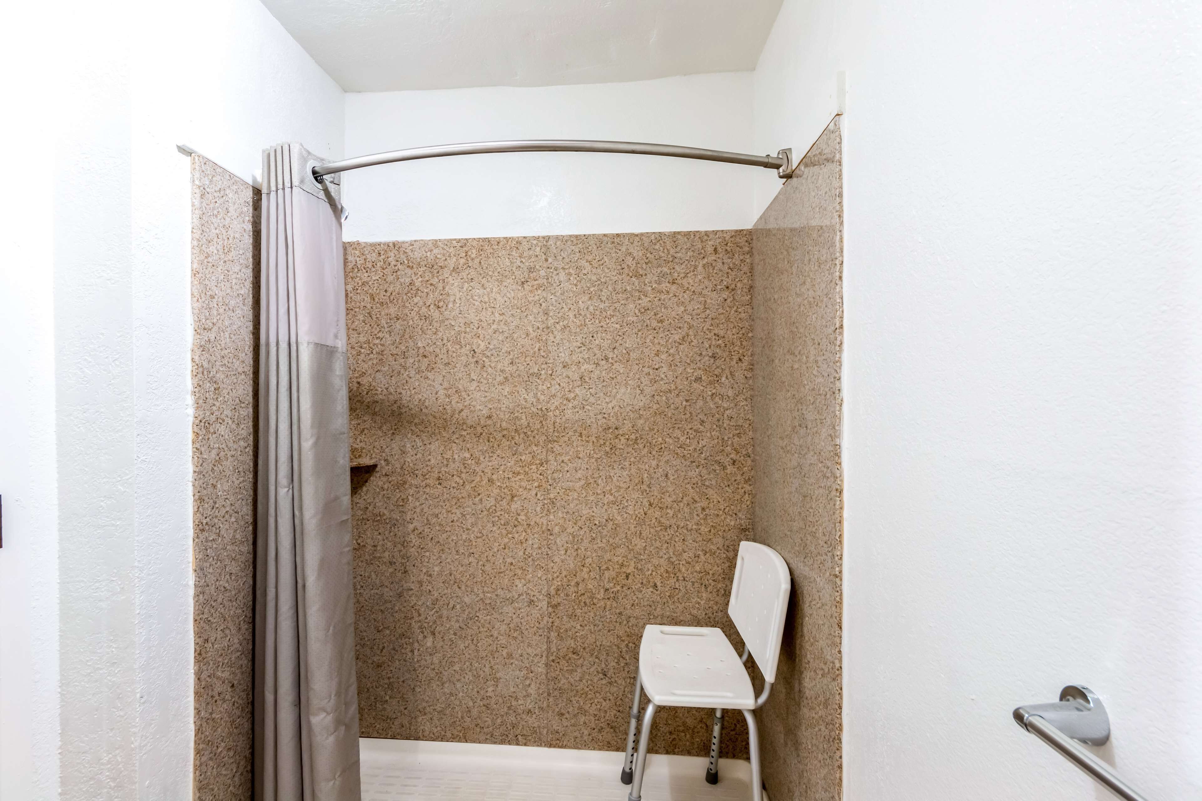 Un área de ducha con cortina, una silla blanca y un perchero.