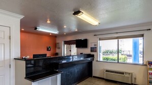 A reception area with a black counter, a flat-screen TV, a window with blinds, and a wall-mounted air conditioning unit.