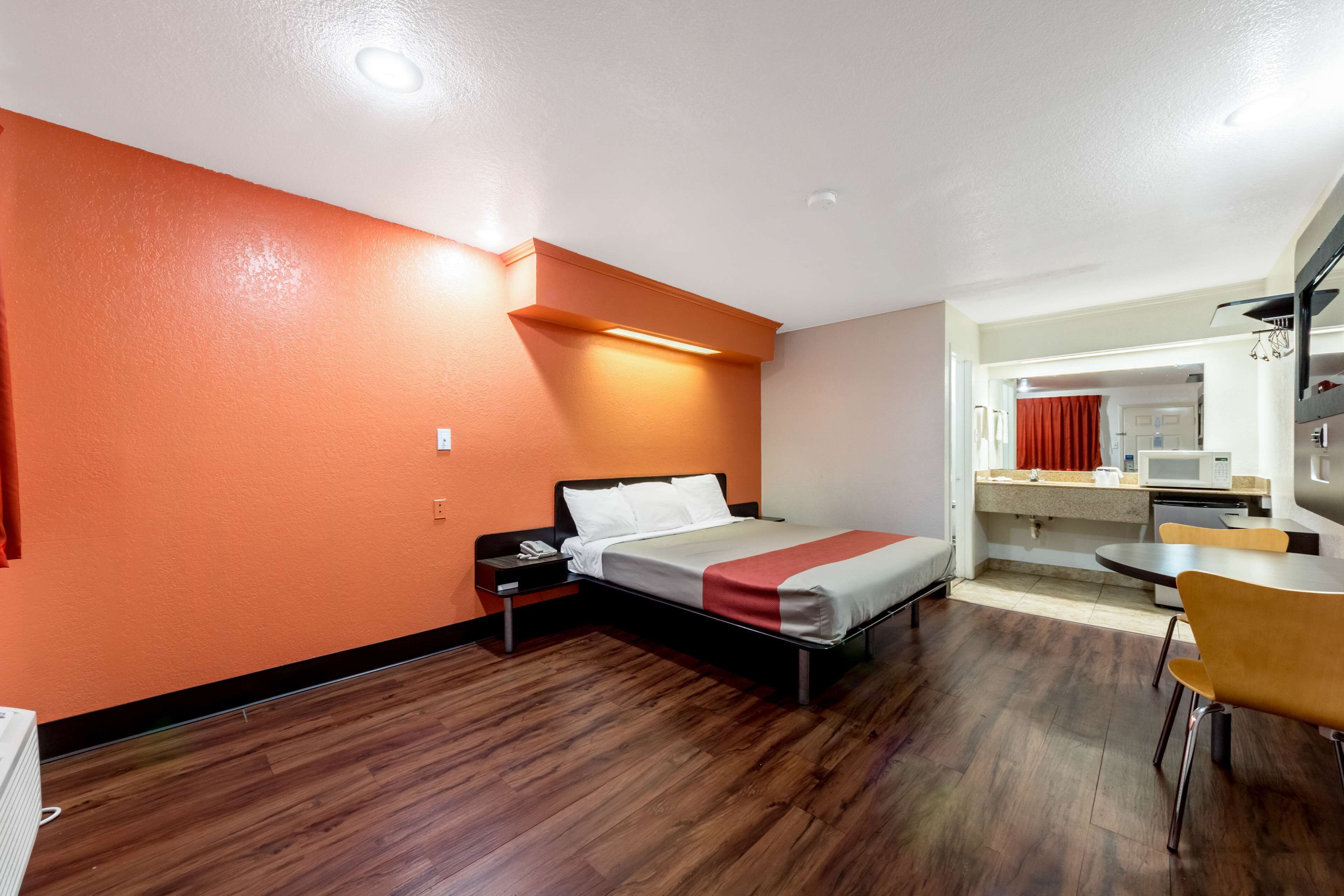 A hotel room with a bed, a desk, a chair, a microwave, and a small kitchenette.