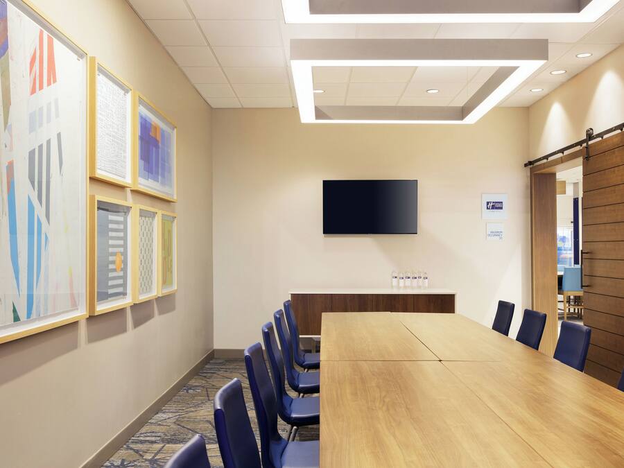 A conference room with a long table, blue chairs, a flat-screen TV, and framed artwork on the walls.