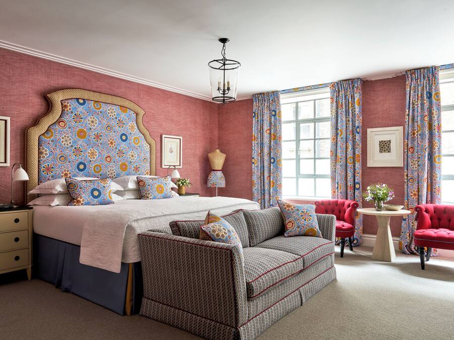 Une chambre à coucher avec un grand lit, un canapé, un fauteuil rouge, une petite table et une fenêtre avec des rideaux.