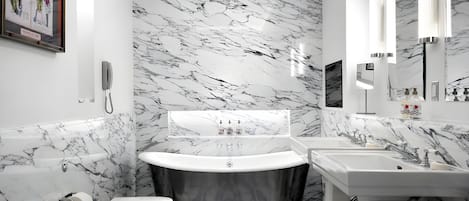 A bathroom with a marble wall, a freestanding bathtub, a toilet, and a sink with a mirror.