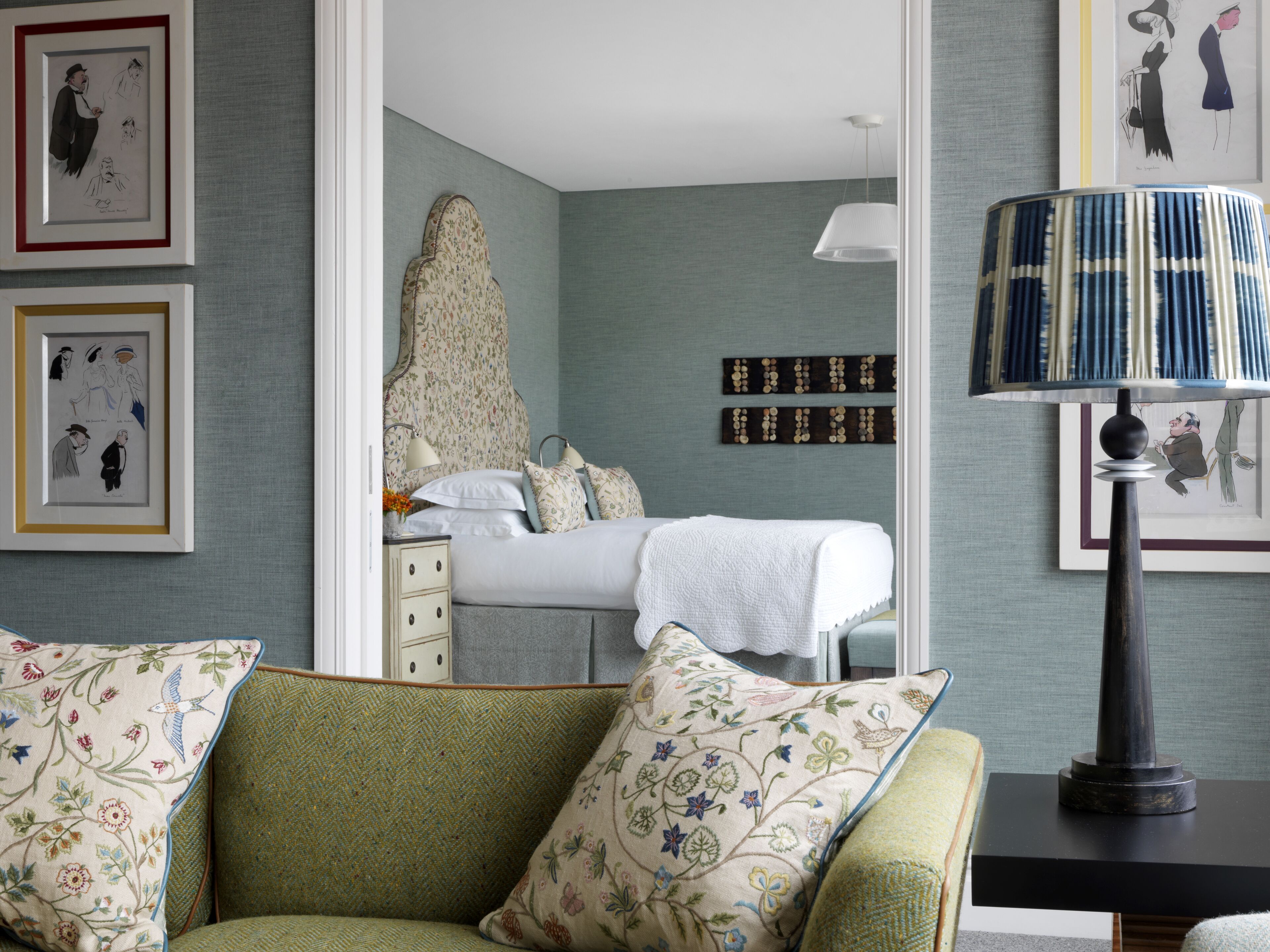 Une chambre à coucher avec un lit, une table de chevet, une lampe et des œuvres d’art encadrées accrochées aux murs.