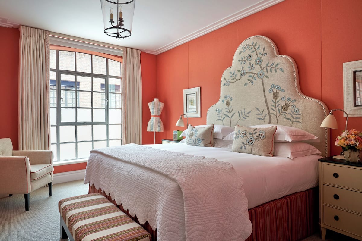 A bedroom with a large bed, a chair, a nightstand, and a window with curtains.