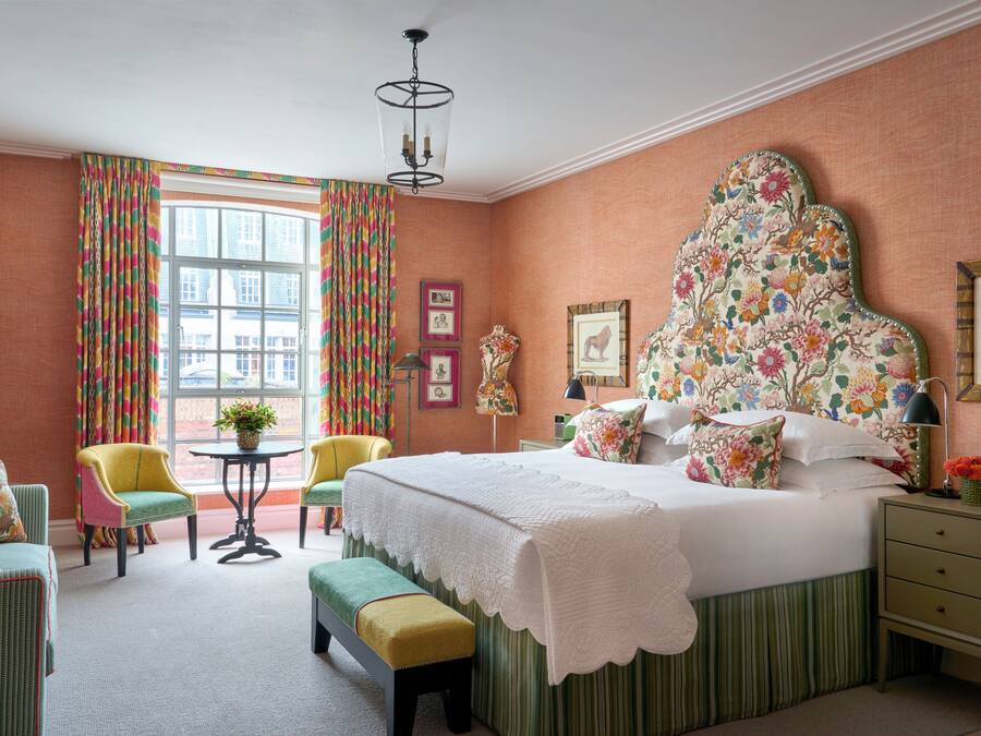 A bedroom with a large bed, a chair, a small table, and a bench.