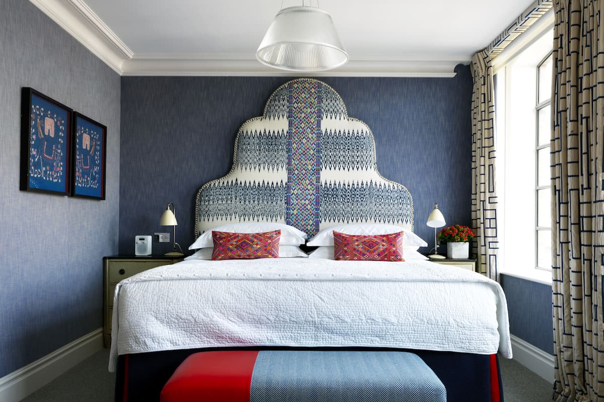 A bedroom with a large bed, two bedside tables, a hanging light fixture, and a window with curtains.
