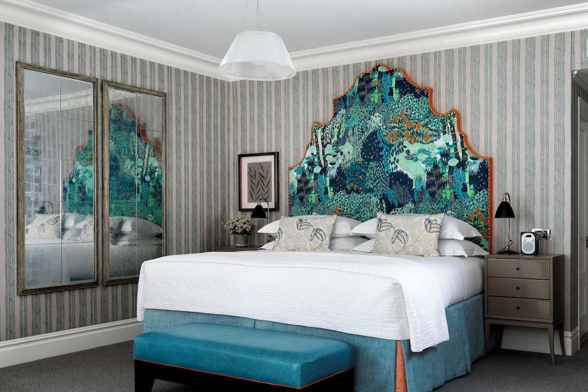 A bedroom with a large bed, a bench, a nightstand, a mirror, and a tapestry on the wall.