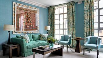 A room with a green sofa, two armchairs, a coffee table, and a large window with curtains.