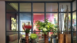 Une pièce avec une table basse en verre, deux plantes en pot et un présentoir à plantes en bois.
