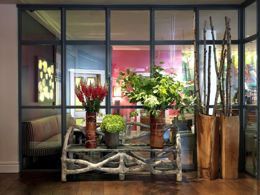 A room with a glass coffee table, two potted plants, and a wooden plant stand.