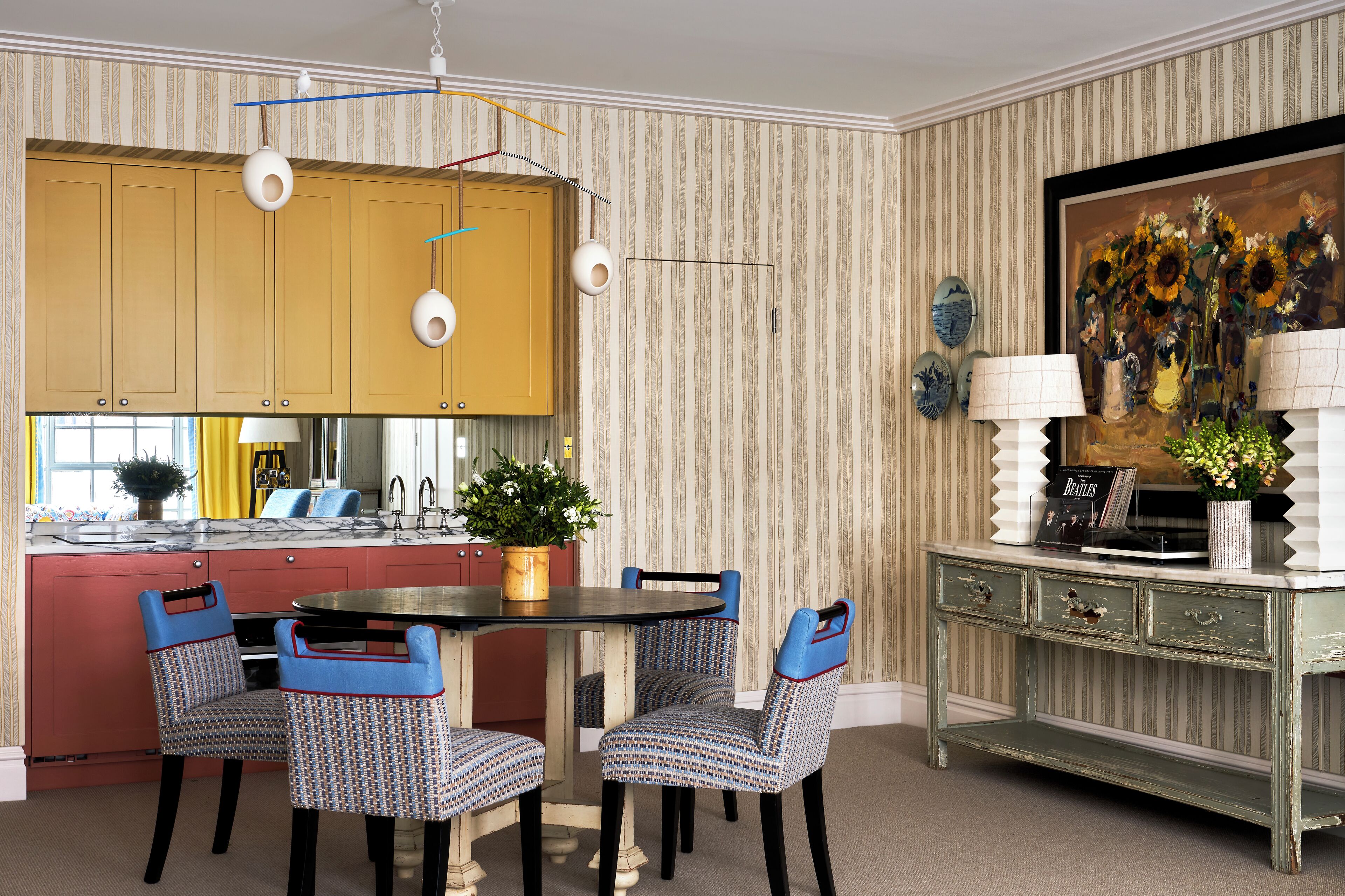 Un coin repas avec un papier peint à rayures, un buffet jaune et des chaises à motifs.