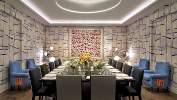 Uma sala de jantar com uma mesa comprida posta para seis pessoas, rodeada por cadeiras estofadas azuis.