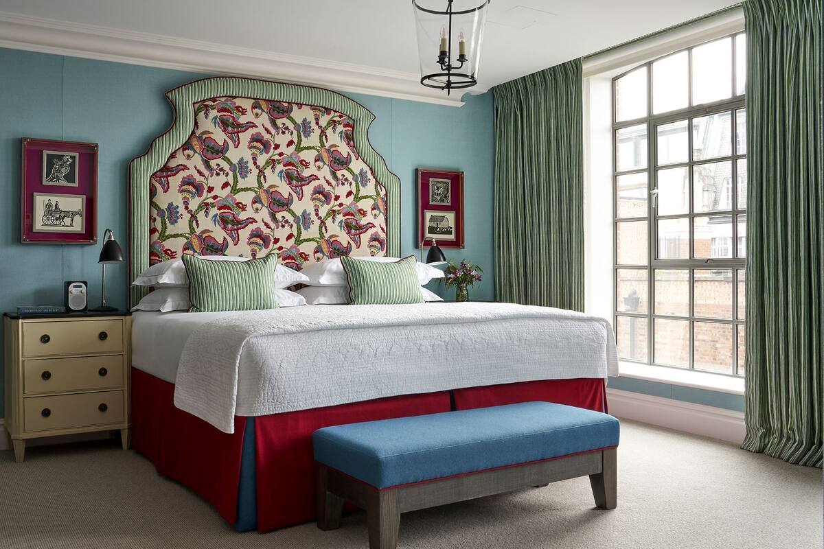 A bedroom with a large bed, a bedside table, a bench, and a window with curtains.