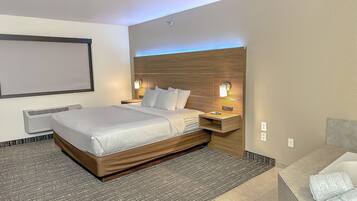 Quarto de hotel com uma cama grande, uma mesinha de cabeceira com abajur, televisão fixada na parede e banheiro com banheira.