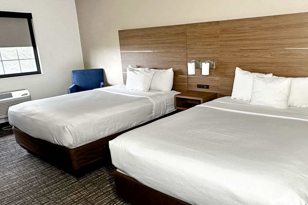 Een hotelkamer met twee bedden, een houten hoofdeinde, een nachtkastje, een stoel en een raam met luiken.