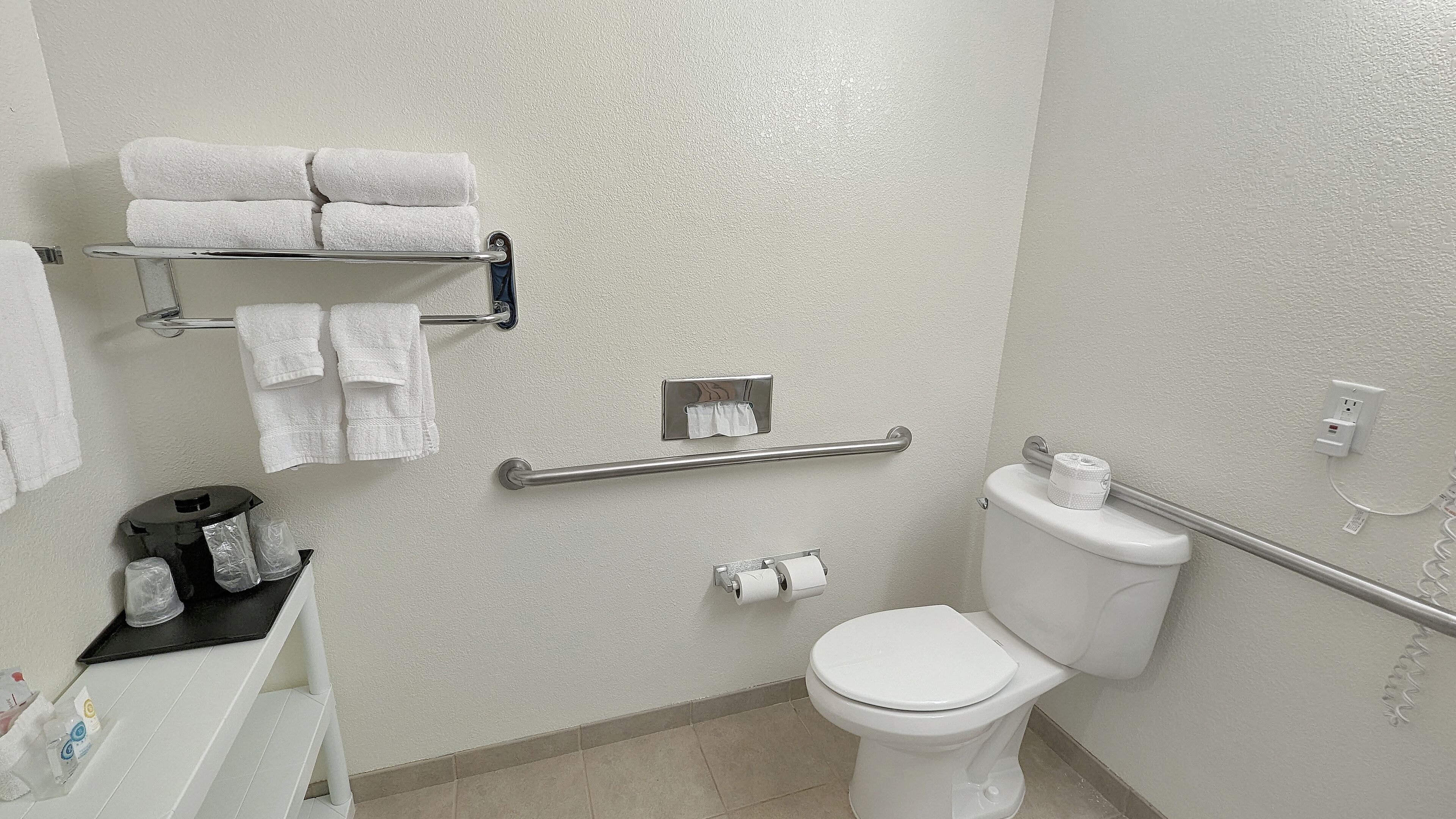 Un baño con inodoro, toallero con toallas dobladas, dispensador de papel higiénico y baranda.