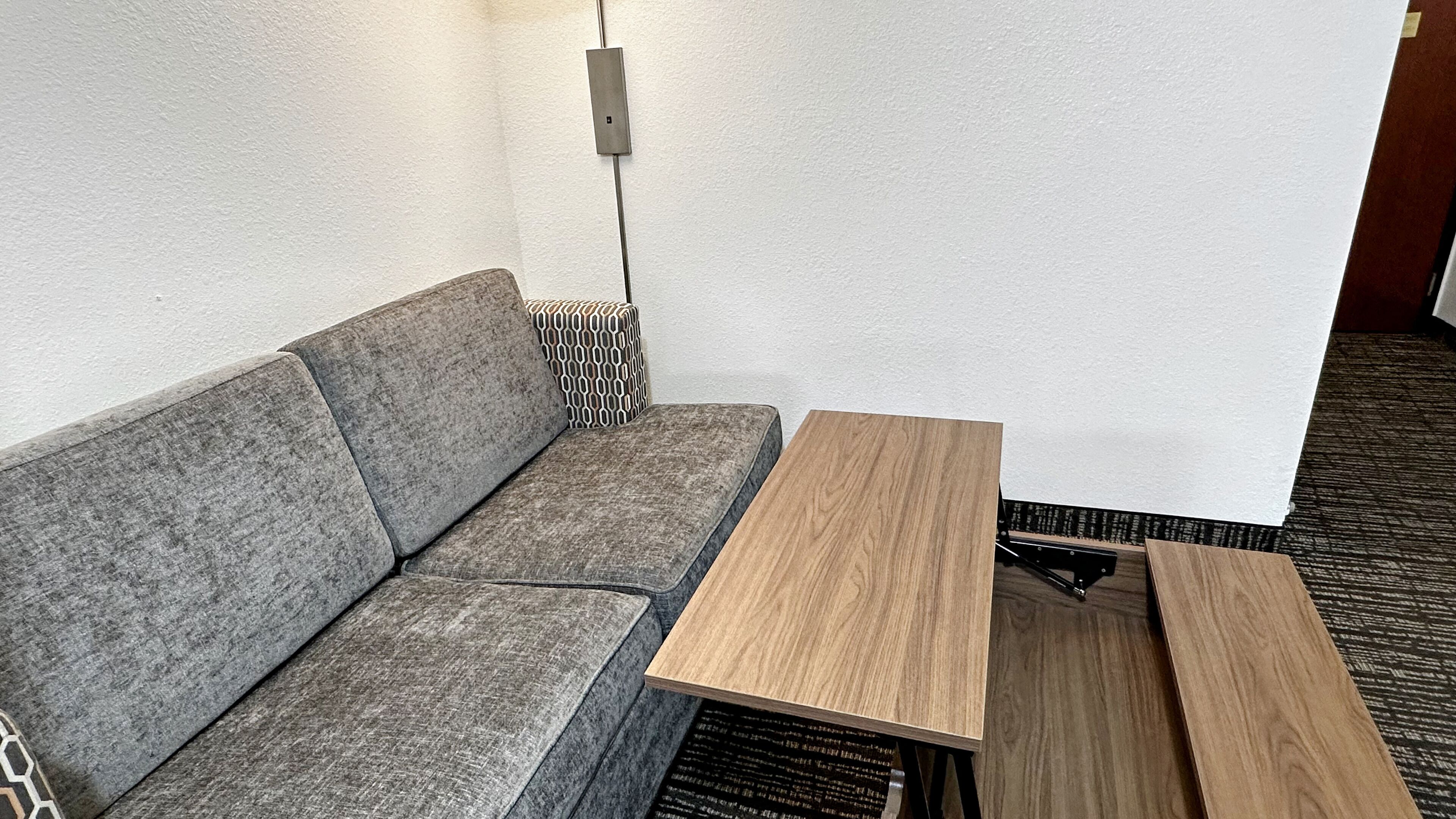 Ein modernes Zimmer mit einem grauen Sofa, einem Holznachttisch und einem gemusterten Teppich.