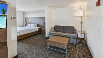 A hotel room with a bed, a sofa, a coffee table, a TV, a lamp, and a fire alarm.